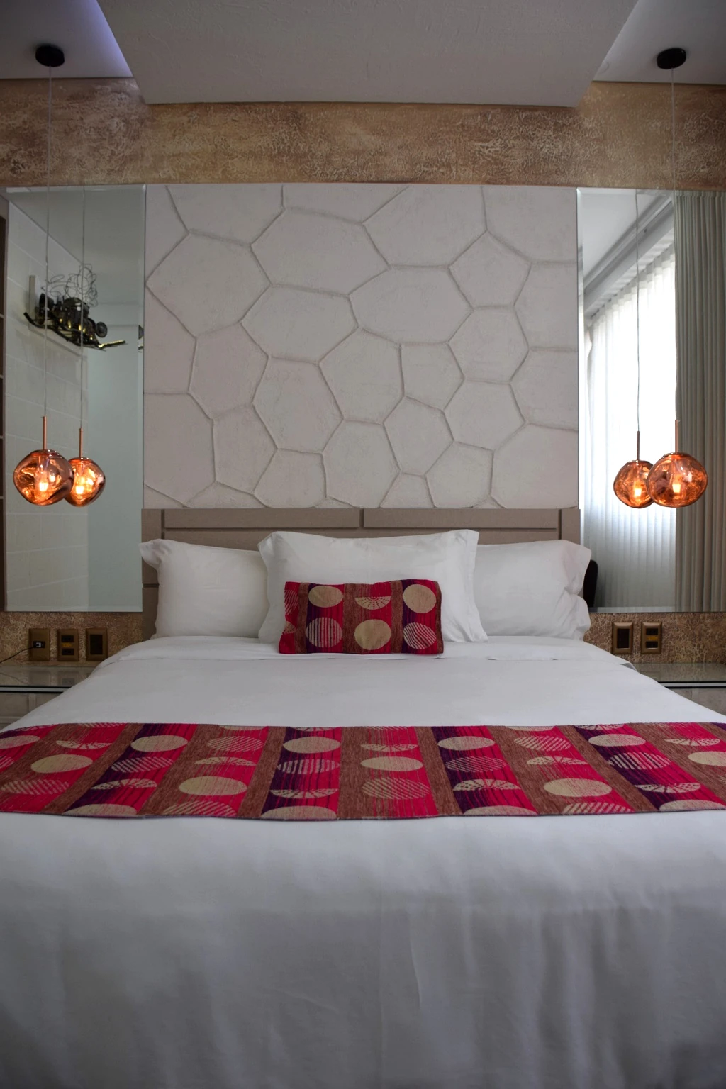 Hotel bedroom with patterned bedding, copper pendant lights and a textured feature wall