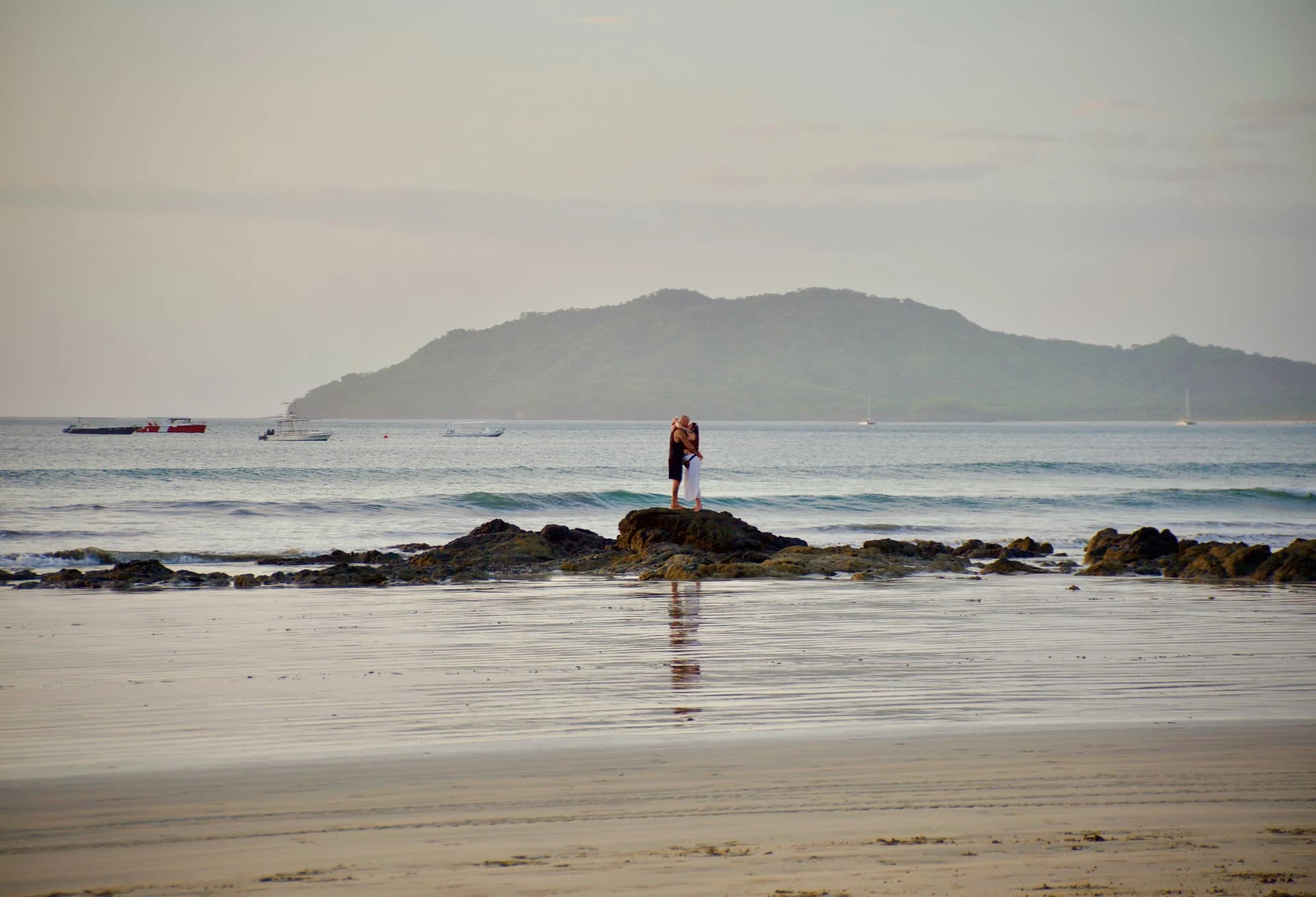 A quiet beach and rocky shoreline with distant mountains in soft evening light